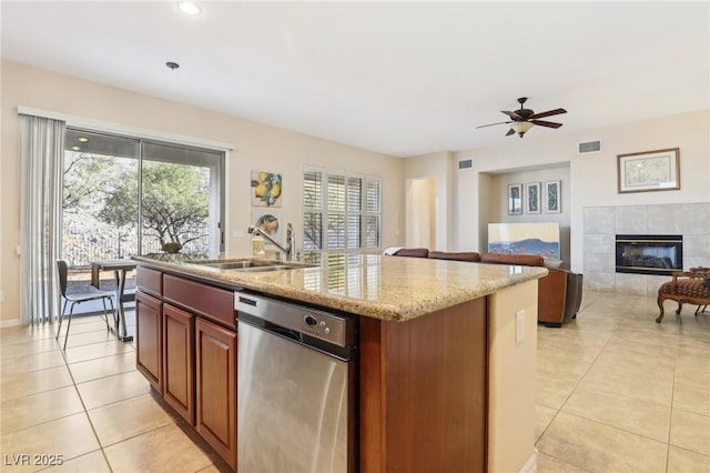 kitchen featuring sink, light tile patterned floors, a kitchen island with sink, light stone counters, and a fireplace