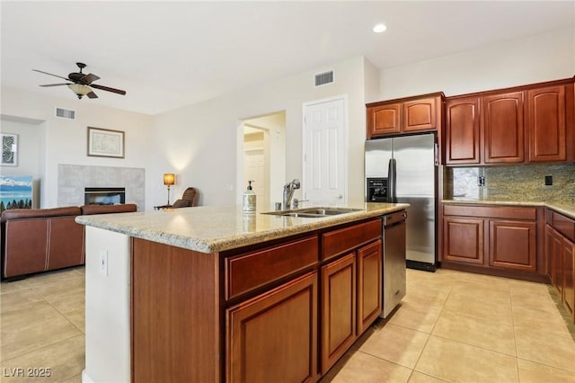 kitchen with sink, light tile patterned floors, a kitchen island with sink, stainless steel appliances, and a tiled fireplace