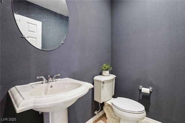 half bathroom with toilet, a textured wall, baseboards, and a sink