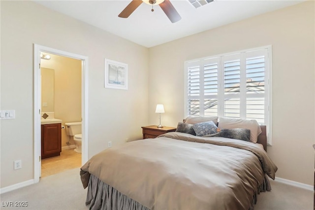 bedroom featuring ceiling fan, light colored carpet, and ensuite bath