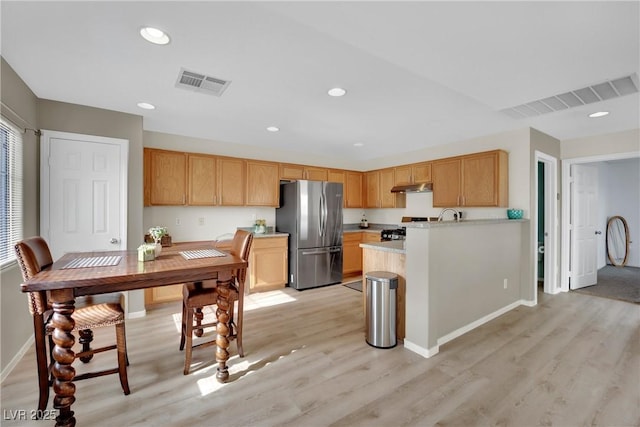 kitchen with light countertops, freestanding refrigerator, visible vents, and under cabinet range hood