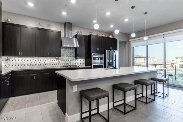 kitchen featuring wall chimney exhaust hood, stainless steel appliances, a kitchen island with sink, and a breakfast bar area