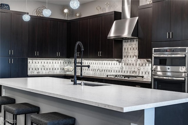 kitchen featuring sink, a breakfast bar area, hanging light fixtures, appliances with stainless steel finishes, and wall chimney range hood