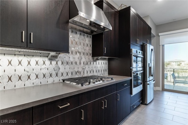 kitchen with light tile patterned flooring, appliances with stainless steel finishes, tasteful backsplash, exhaust hood, and dark brown cabinets