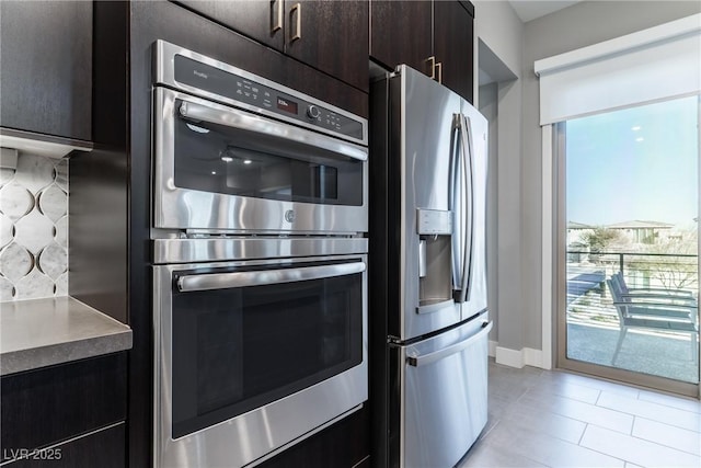 kitchen featuring backsplash, dark brown cabinets, light tile patterned flooring, and appliances with stainless steel finishes