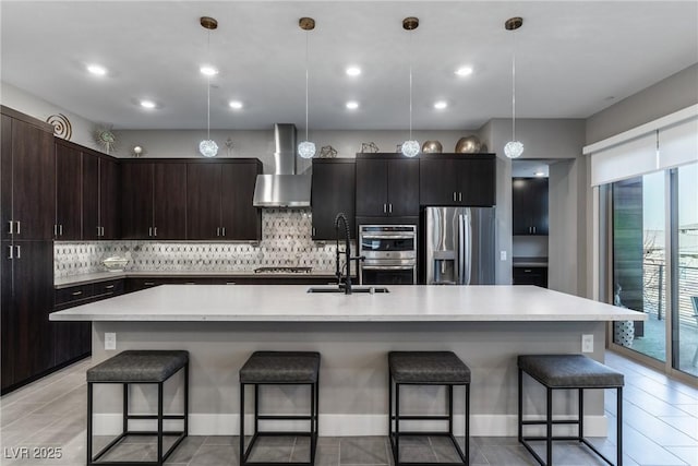 kitchen with tasteful backsplash, appliances with stainless steel finishes, light countertops, wall chimney range hood, and a sink