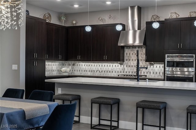 kitchen with wall chimney range hood, a breakfast bar, stainless steel double oven, and light countertops