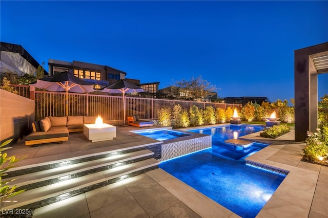 pool at night with an in ground hot tub, a patio area, and a fire pit