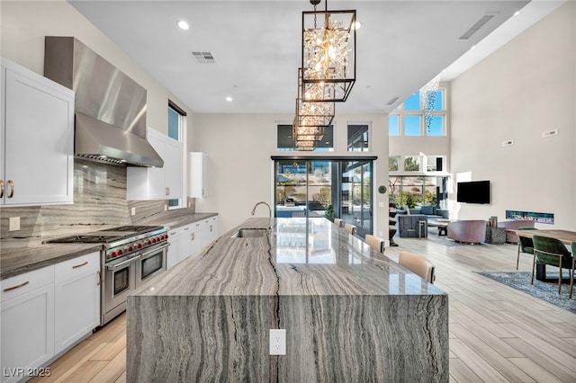 kitchen with double oven range, light stone countertops, wall chimney range hood, and white cabinets