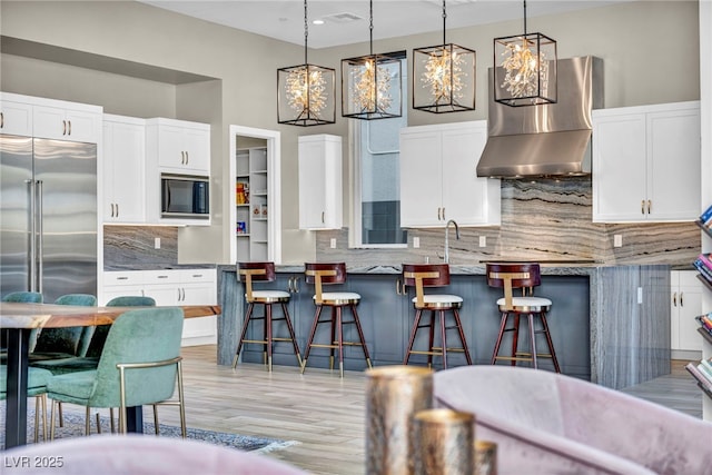 kitchen with built in appliances, extractor fan, white cabinetry, and a kitchen bar