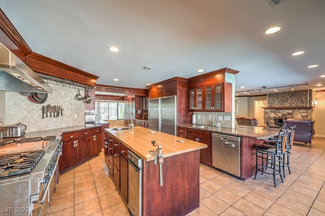 kitchen featuring glass insert cabinets, premium appliances, a center island with sink, and a sink