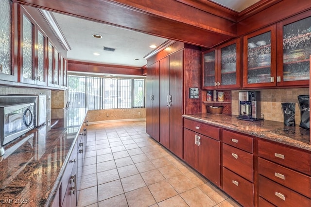 kitchen with glass insert cabinets, stainless steel microwave, dark stone countertops, and ornamental molding