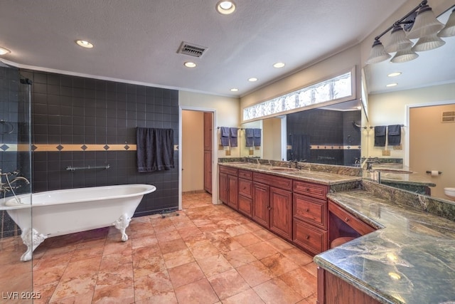 bathroom featuring visible vents, a soaking tub, a textured ceiling, vanity, and tile walls