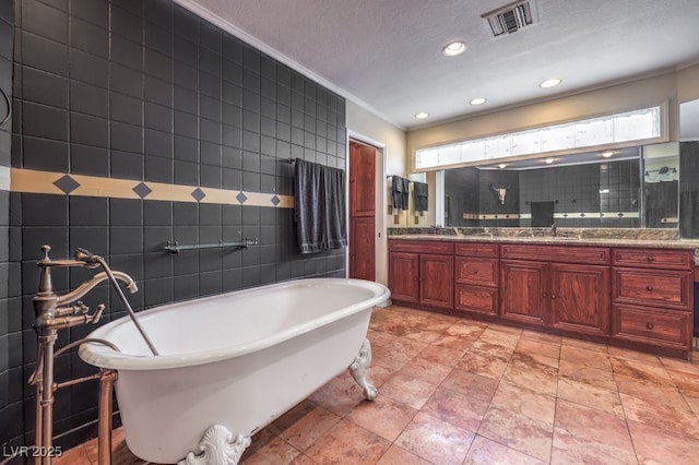 full bath featuring double vanity, visible vents, a soaking tub, a textured ceiling, and tile walls