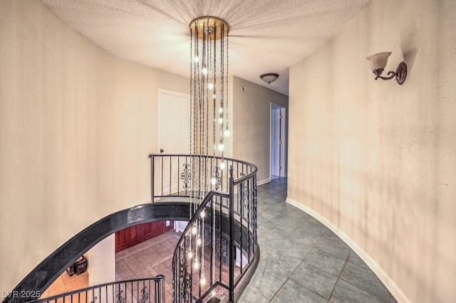 hallway featuring a textured ceiling, arched walkways, an upstairs landing, and baseboards