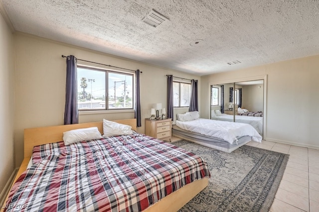 bedroom featuring visible vents, a textured ceiling, baseboards, and light tile patterned floors