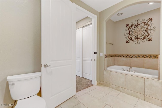 bathroom with toilet, tiled bath, and tile patterned flooring