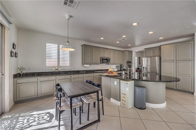 kitchen with light tile patterned flooring, appliances with stainless steel finishes, a kitchen island with sink, and hanging light fixtures