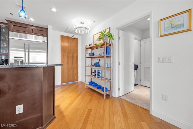 kitchen with built in refrigerator, an inviting chandelier, light wood-type flooring, and dark stone counters