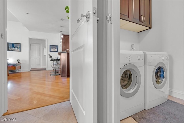 clothes washing area with cabinets, washing machine and dryer, and light wood-type flooring