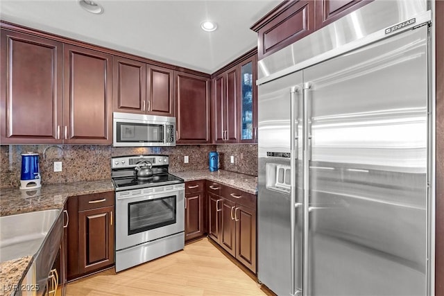 kitchen with tasteful backsplash, light stone countertops, stainless steel appliances, and light wood-type flooring