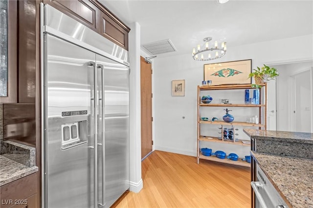 kitchen with stainless steel built in refrigerator, light stone countertops, an inviting chandelier, and light hardwood / wood-style flooring