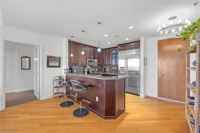 kitchen featuring hanging light fixtures, light wood-type flooring, appliances with stainless steel finishes, kitchen peninsula, and backsplash