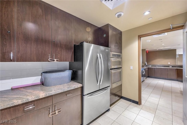 kitchen featuring backsplash, stainless steel appliances, light tile patterned floors, and dark stone counters