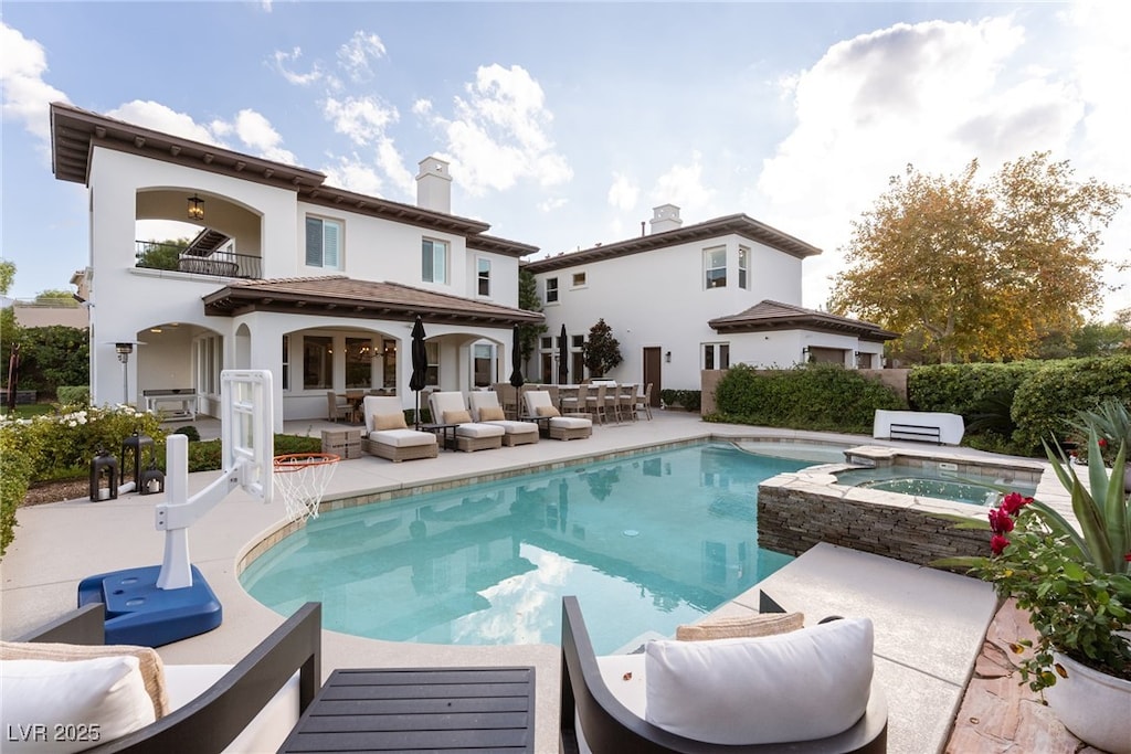 rear view of property with a balcony, an outdoor hangout area, a pool with hot tub, and a patio area