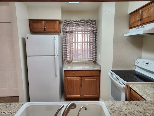 kitchen with light stone counters, white appliances, and sink