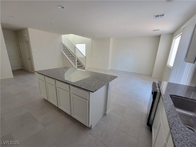 kitchen with white cabinetry, dark stone counters, sink, and a kitchen island