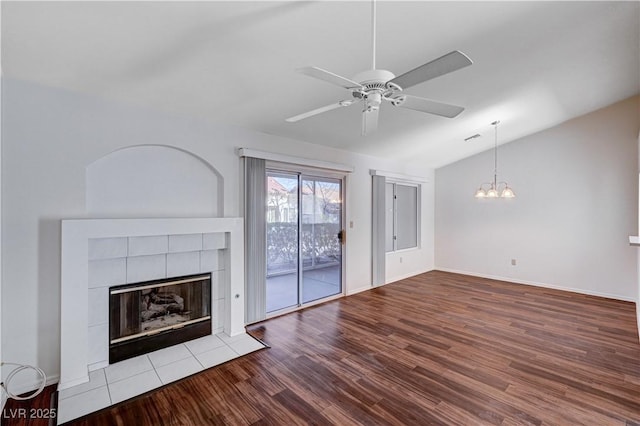 unfurnished living room featuring vaulted ceiling, ceiling fan with notable chandelier, light hardwood / wood-style floors, and a tile fireplace