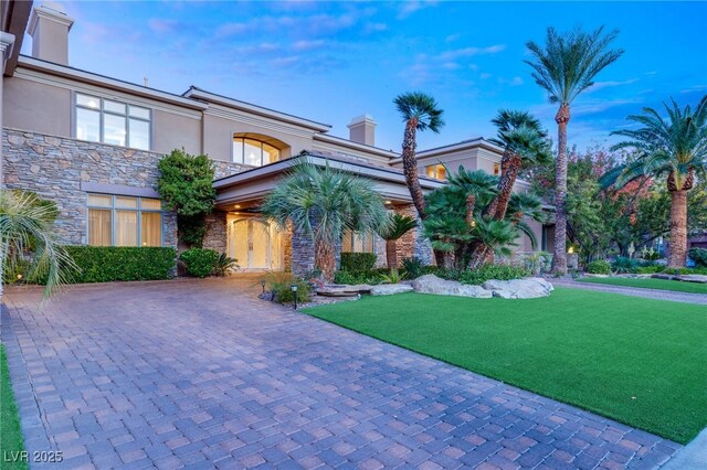 1549 Foothills Village Dr, Henderson, NV 89012 - view of front of home featuring a front lawn, stone siding, curved driveway, stucco siding, and a chimney