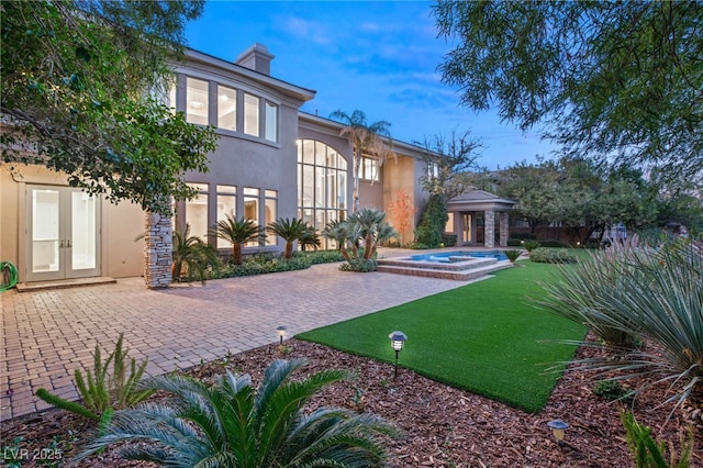 rear view of property with an in ground hot tub, a yard, and a patio area