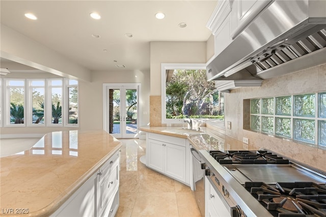 kitchen with sink, range hood, light stone counters, white cabinets, and decorative backsplash