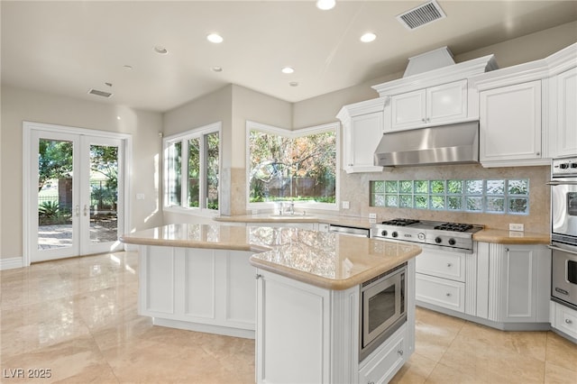 kitchen with tasteful backsplash, a center island, stainless steel appliances, light stone countertops, and white cabinets