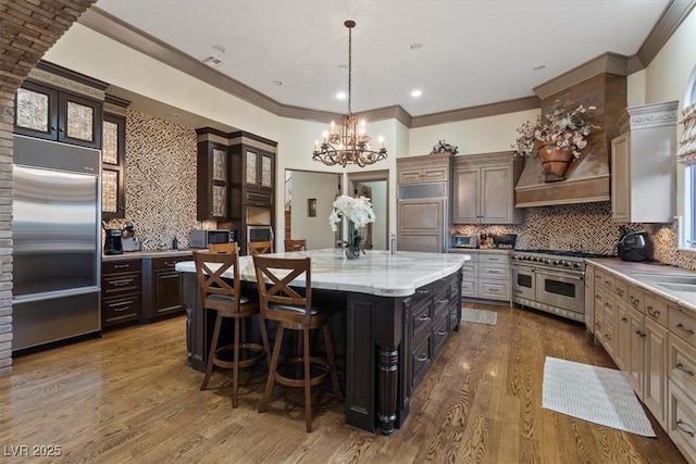 kitchen featuring a center island, high quality appliances, dark brown cabinetry, tasteful backsplash, and a kitchen bar