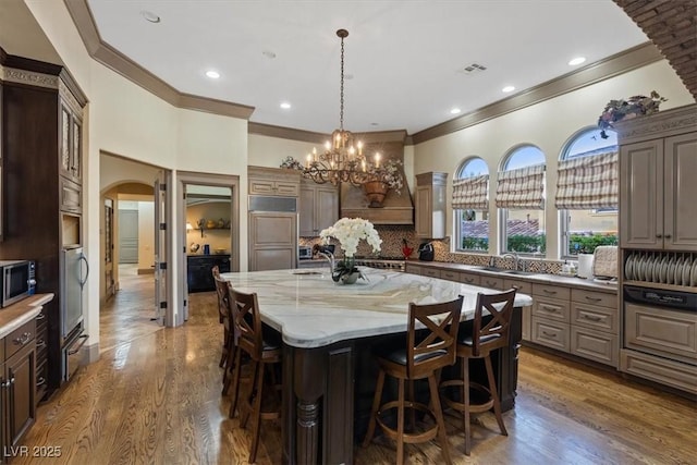 kitchen featuring sink, light stone counters, paneled fridge, an island with sink, and custom exhaust hood