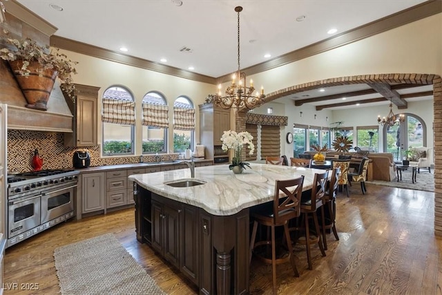 kitchen with light stone counters, double oven range, hardwood / wood-style flooring, and an island with sink