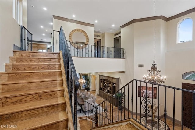 stairs with crown molding, a towering ceiling, and a notable chandelier