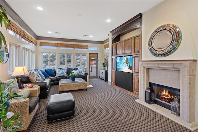 living room featuring a tiled fireplace, crown molding, and light carpet