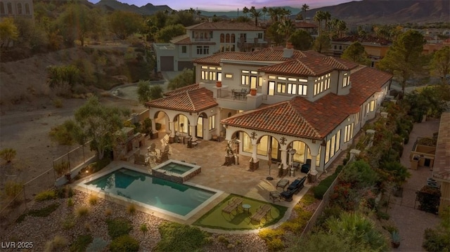 back house at dusk featuring an in ground hot tub, a balcony, and a patio