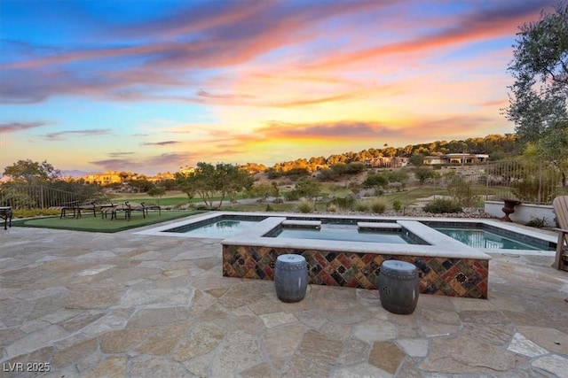 pool at dusk with an in ground hot tub and a patio area