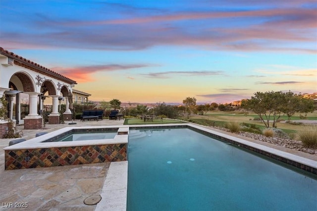 pool at dusk with an in ground hot tub and a patio area