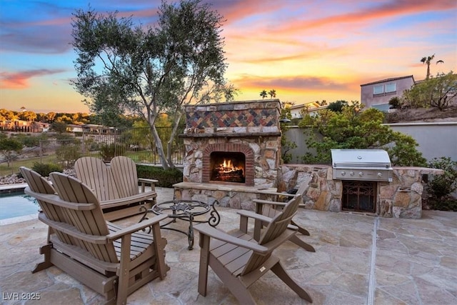 patio terrace at dusk featuring an outdoor kitchen, a grill, and an outdoor stone fireplace