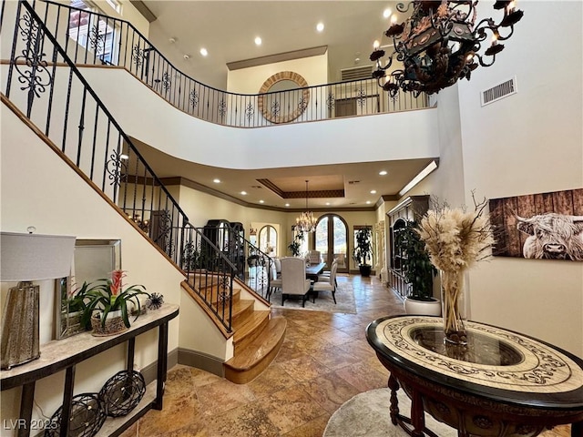 foyer entrance with crown molding, a towering ceiling, a raised ceiling, and a notable chandelier