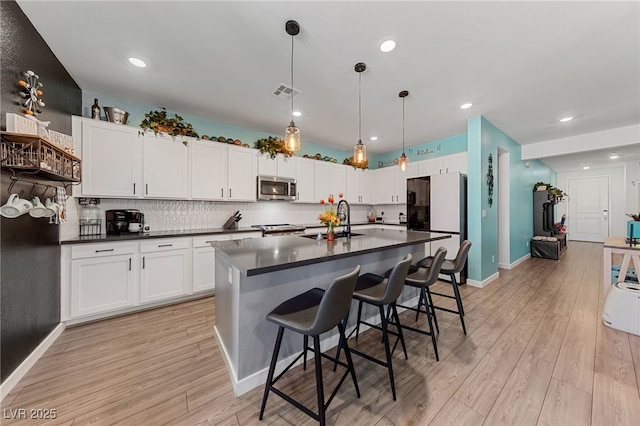 kitchen with appliances with stainless steel finishes, white cabinetry, sink, hanging light fixtures, and a kitchen island with sink