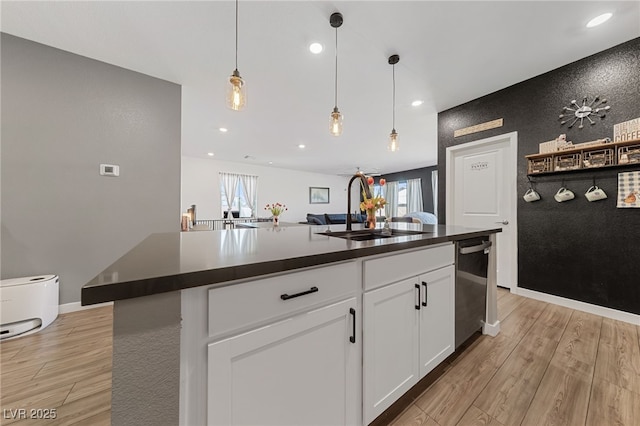 kitchen with sink, stainless steel dishwasher, pendant lighting, a kitchen island with sink, and white cabinets