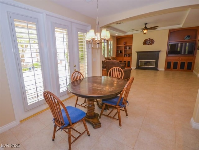 dining area with ceiling fan with notable chandelier, a wealth of natural light, built in features, and a tray ceiling