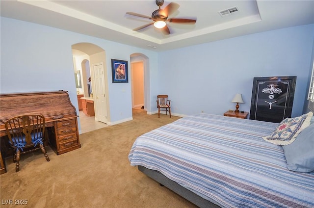 carpeted bedroom featuring a raised ceiling, ceiling fan, and ensuite bath